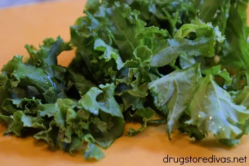 Cut kale slices on an orange cutting board.