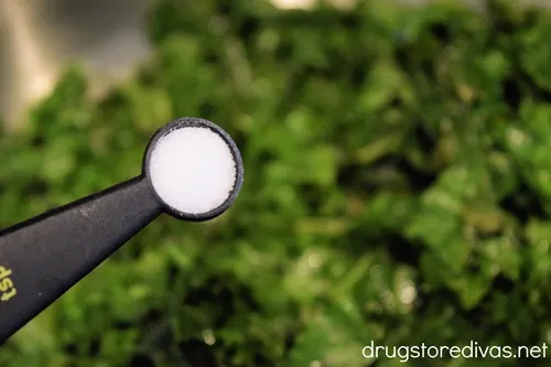 Salt in a measuring spoon above a skillet filled with cooked kale.